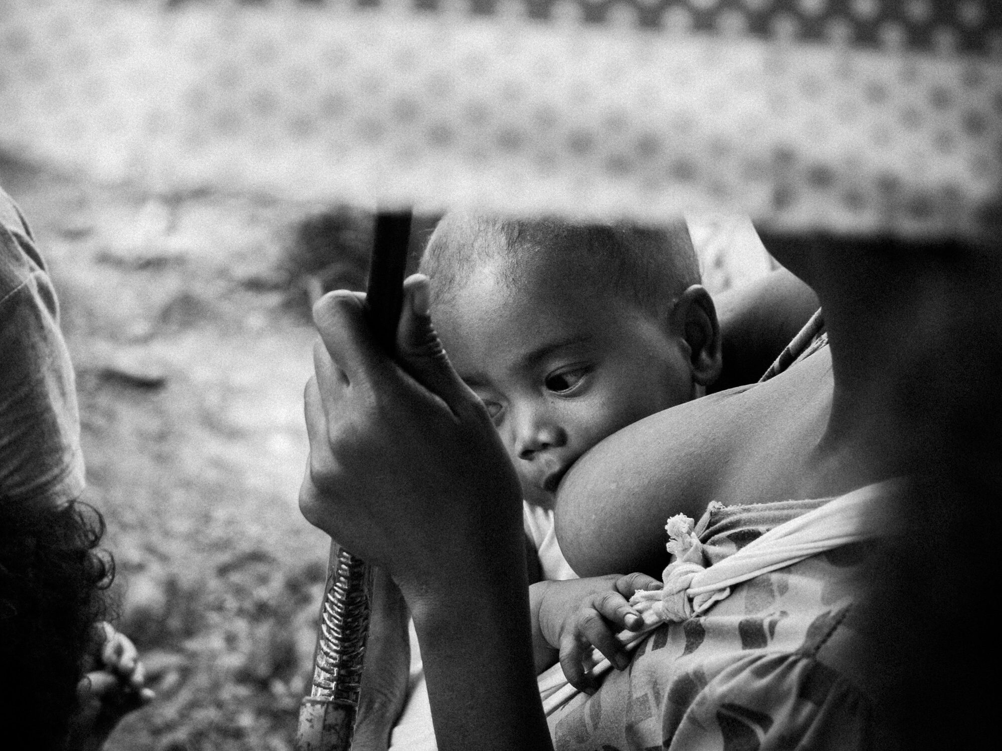 grayscale photo of breastfeeding mother with umbrella